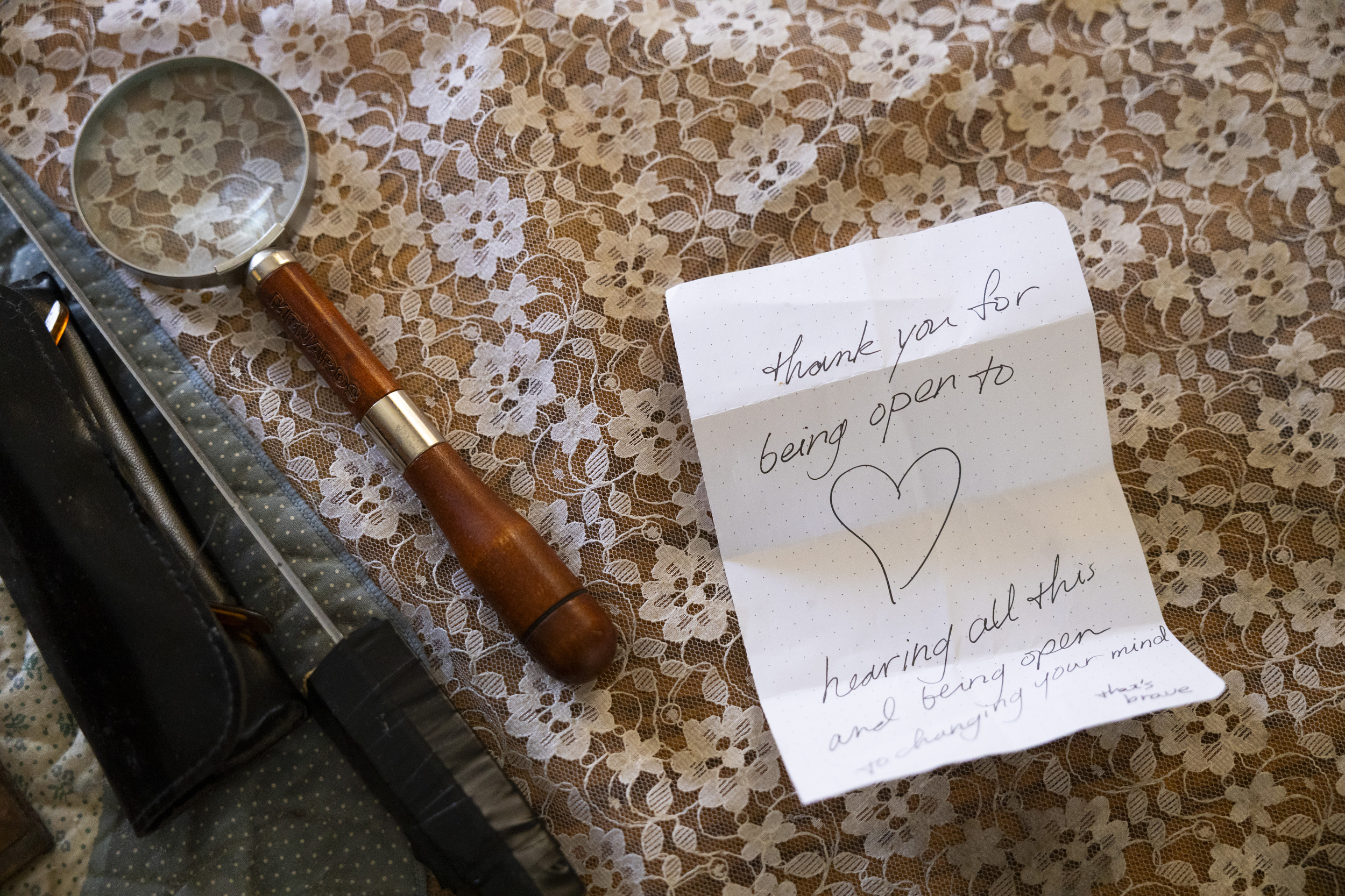 Magnifying glass and case on lace fabric beside a handwritten note with a heart, expressing gratitude for openness and listening.