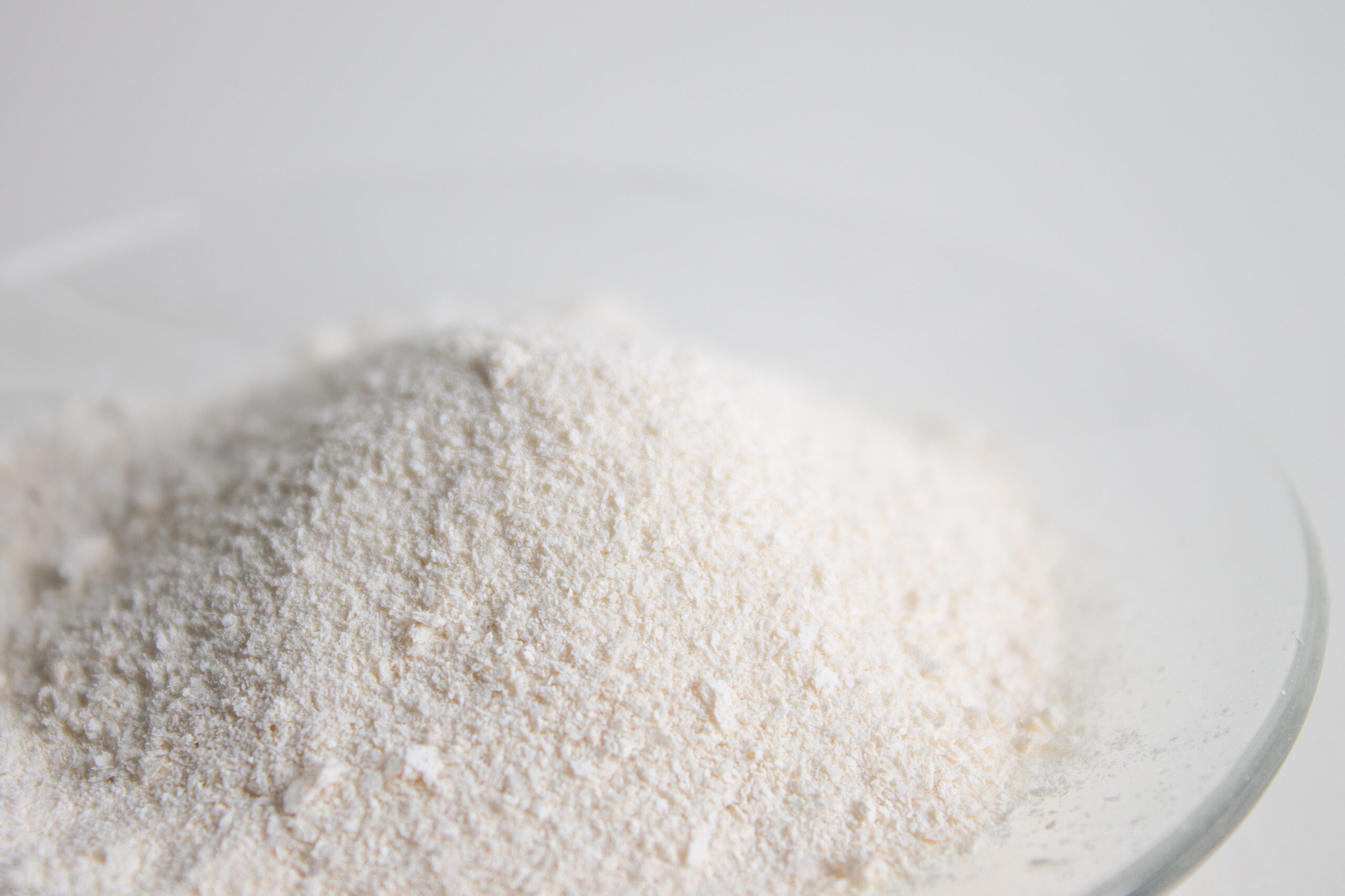 A close-up of a mound of white powder, possibly flour, on a transparent glass plate against a plain white background.